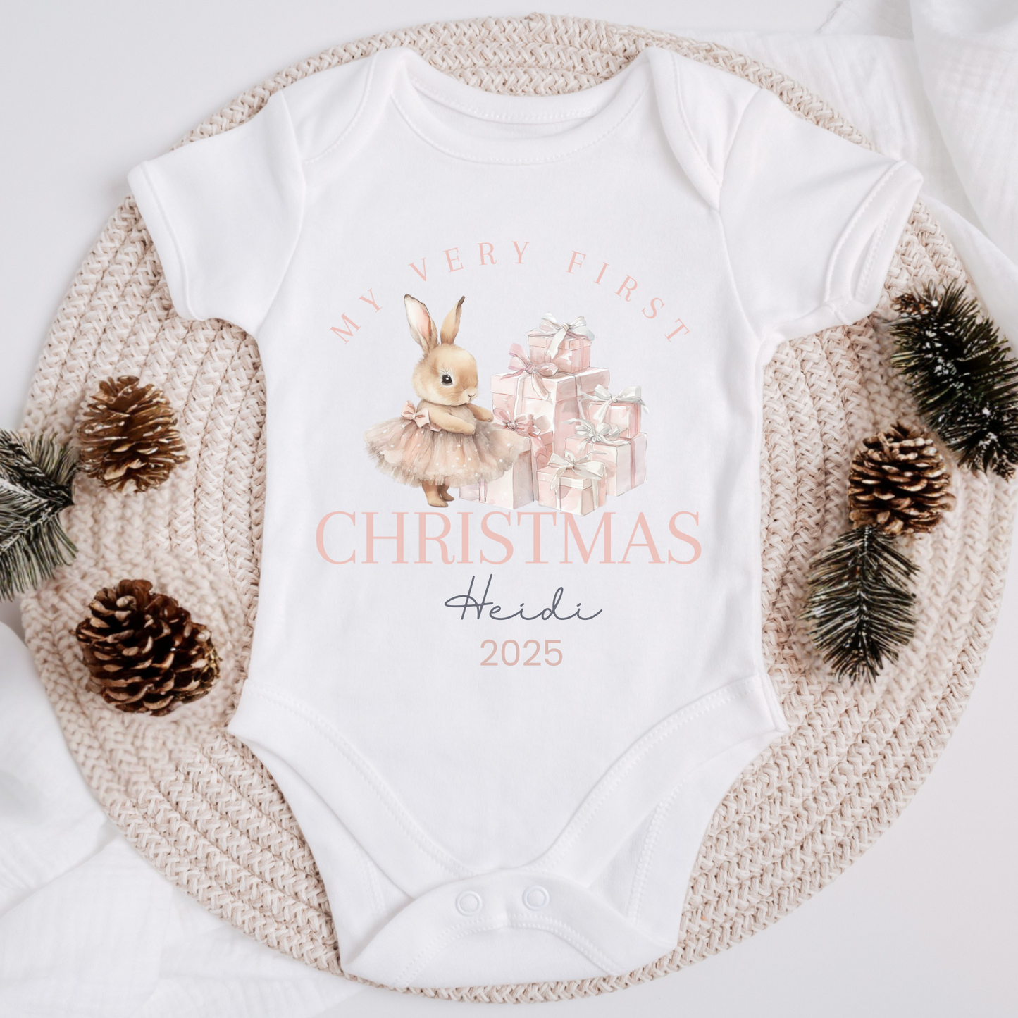 White baby onesie with Christmas design and text, surrounded by decorative elements on a white background.
