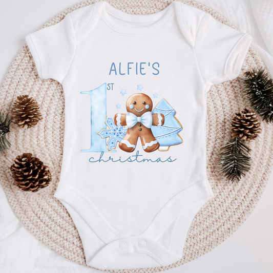 White baby onesie with gingerbread design and text on a textured surface with pinecones and branches.
