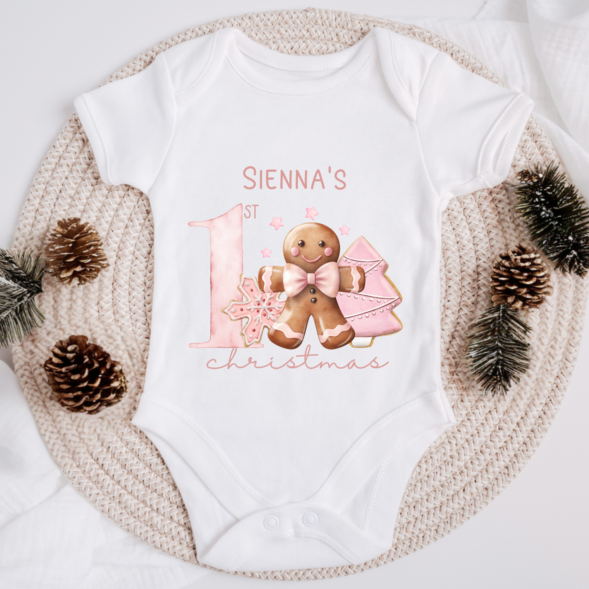 White baby onesie with pink gingerbread design and text saying my first Christmas
