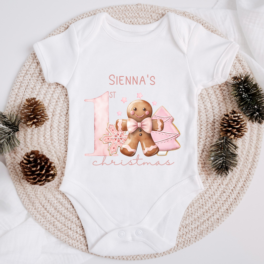 White baby onesie with pink gingerbread design and text saying my first Christmas

