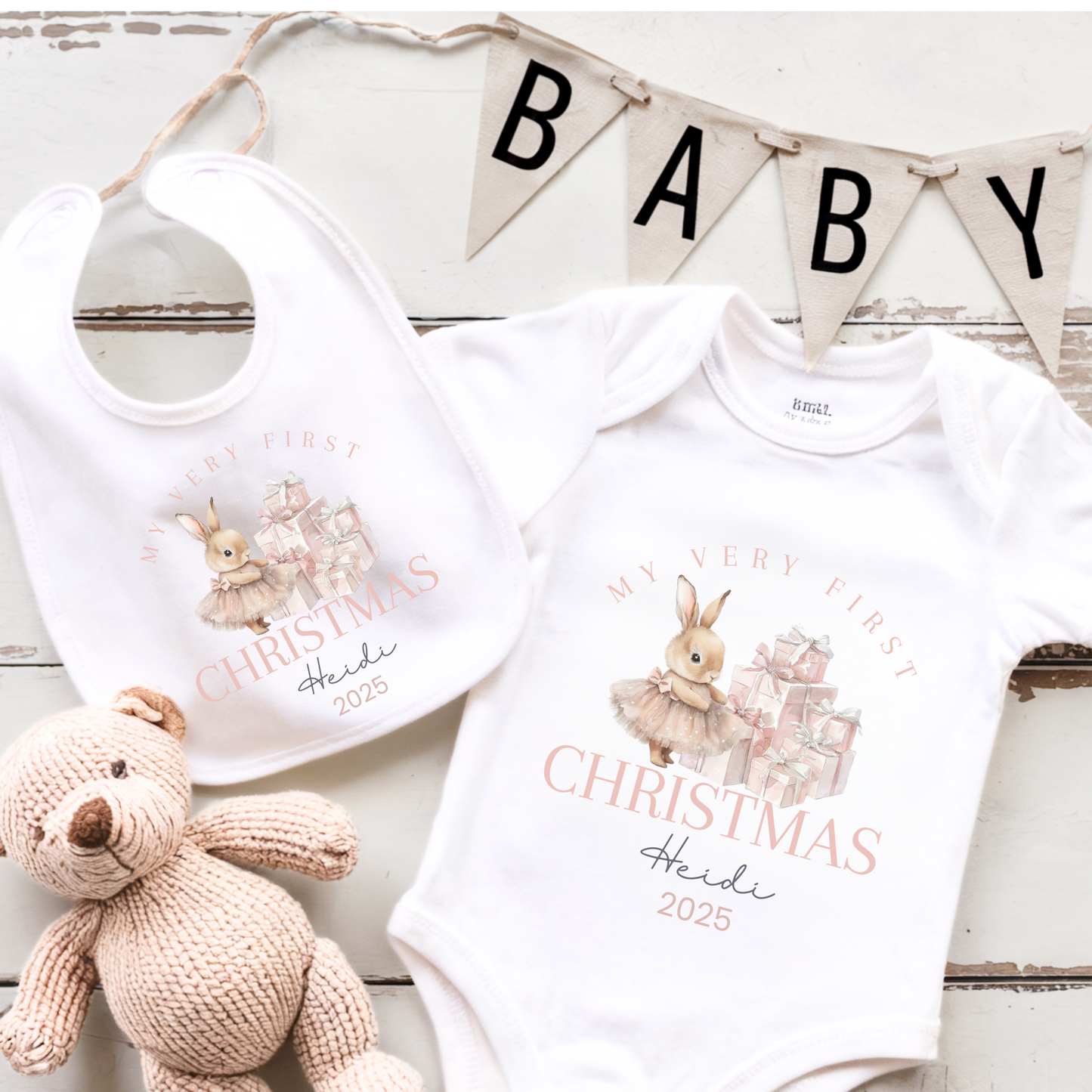 Baby bib and onesie with 'My Very First Christmas' design, accompanied by a plush toy on a wooden surface.