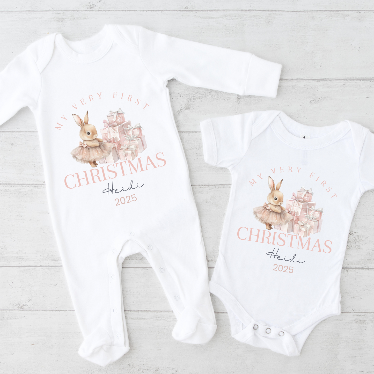 Two baby onesies with Christmas design and text on a light wooden surface