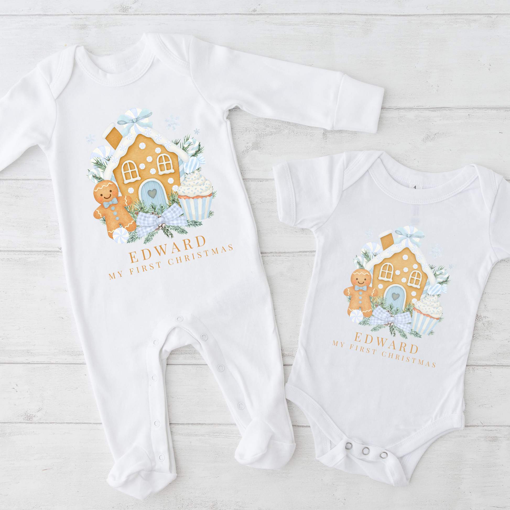 Two baby onesies with gingerbread house design and 'Edward My First Christmas' text on a light wooden surface.