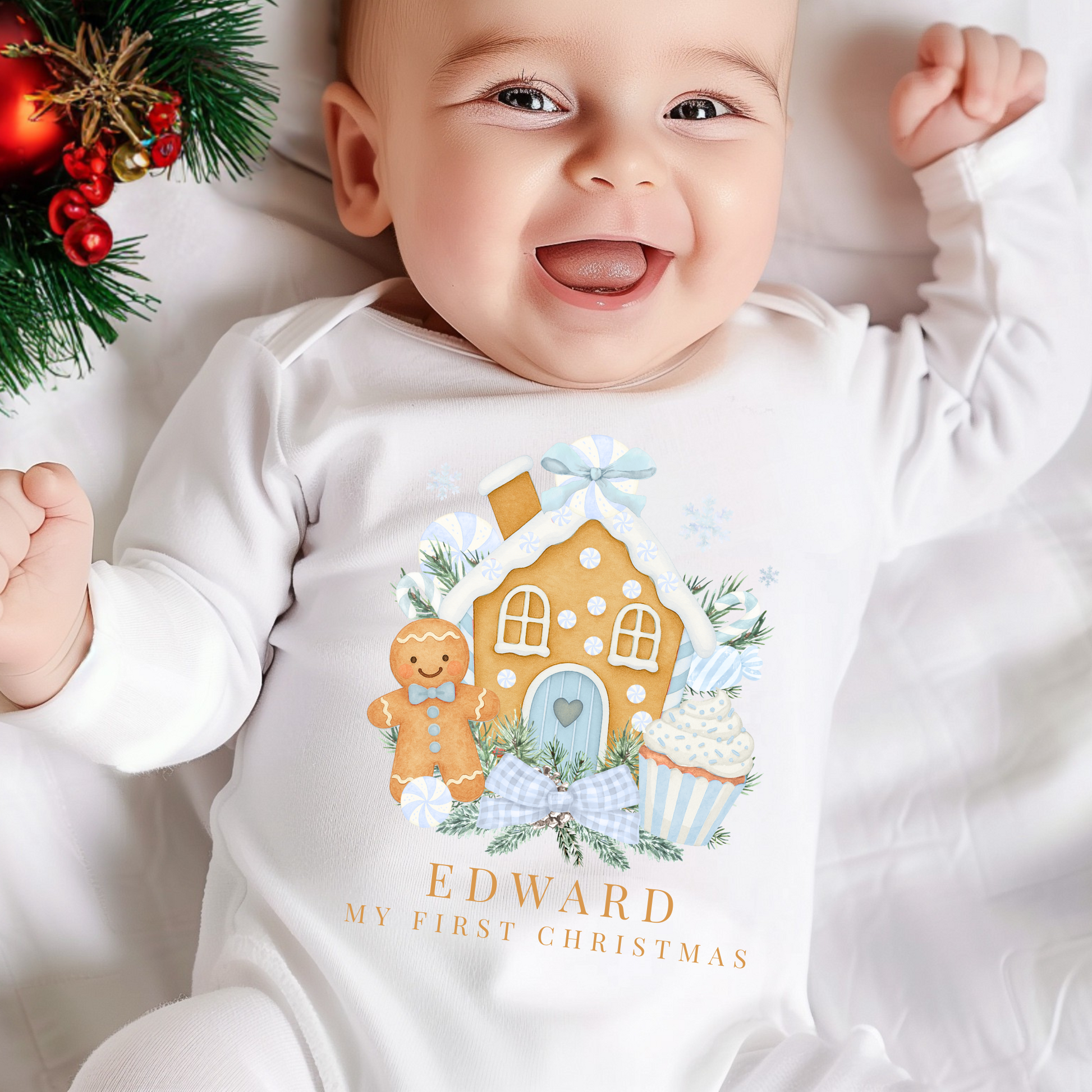 Baby wearing a onesie with a gingerbread house design and text, surrounded by Christmas decorations.