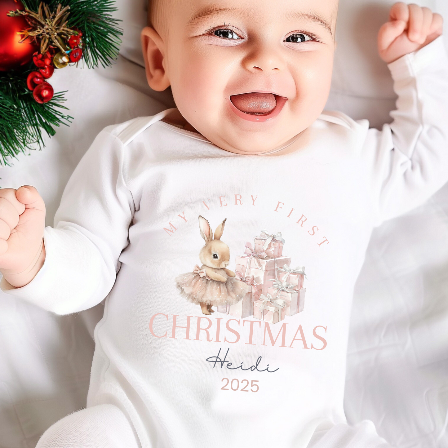 Baby wearing a 'My First Christmas' sleepsuit with festive decorations in the background.