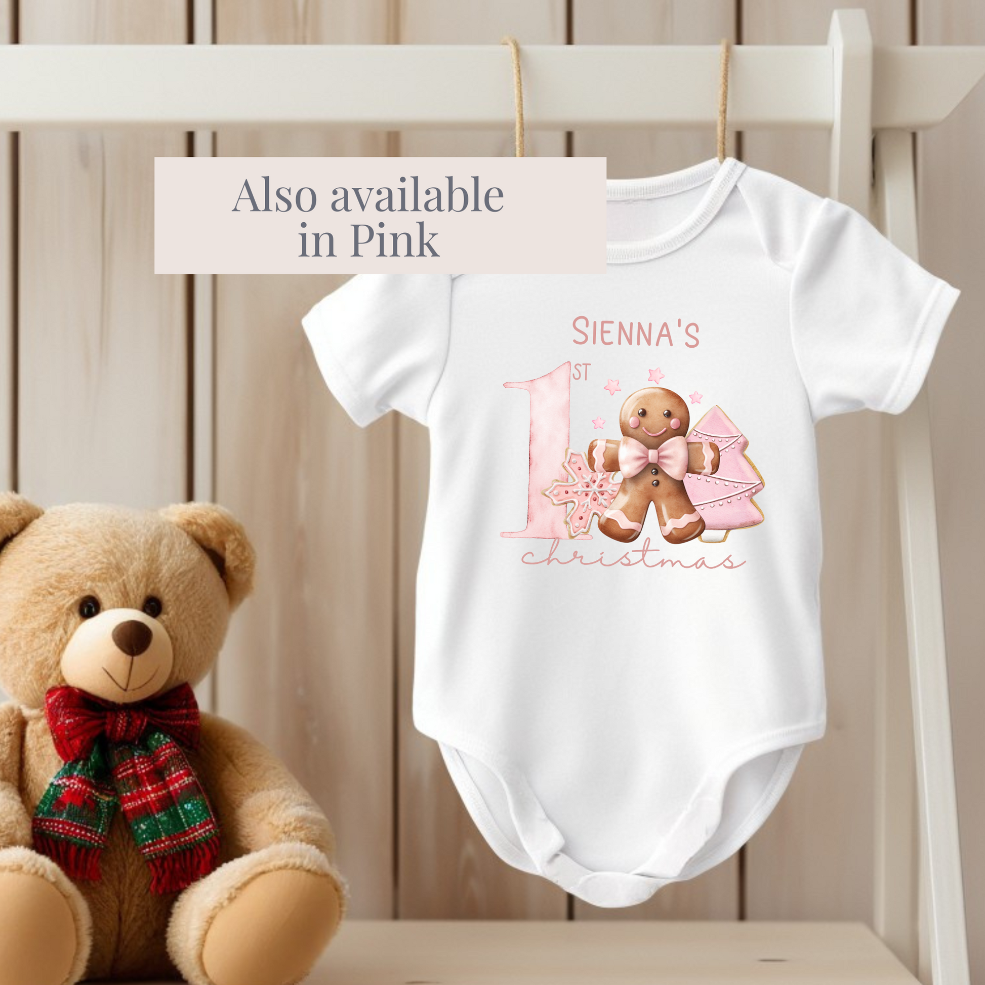 Baby onesie with gingerbread design and name, next to a teddy bear on a wooden surface.