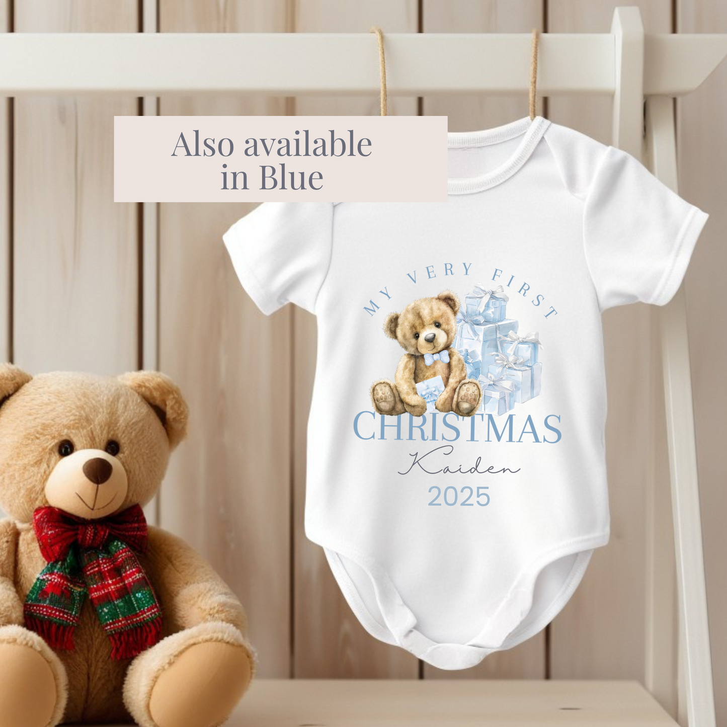 Baby onesie with teddy bear design and text, next to a teddy bear with a red scarf on a wooden background.